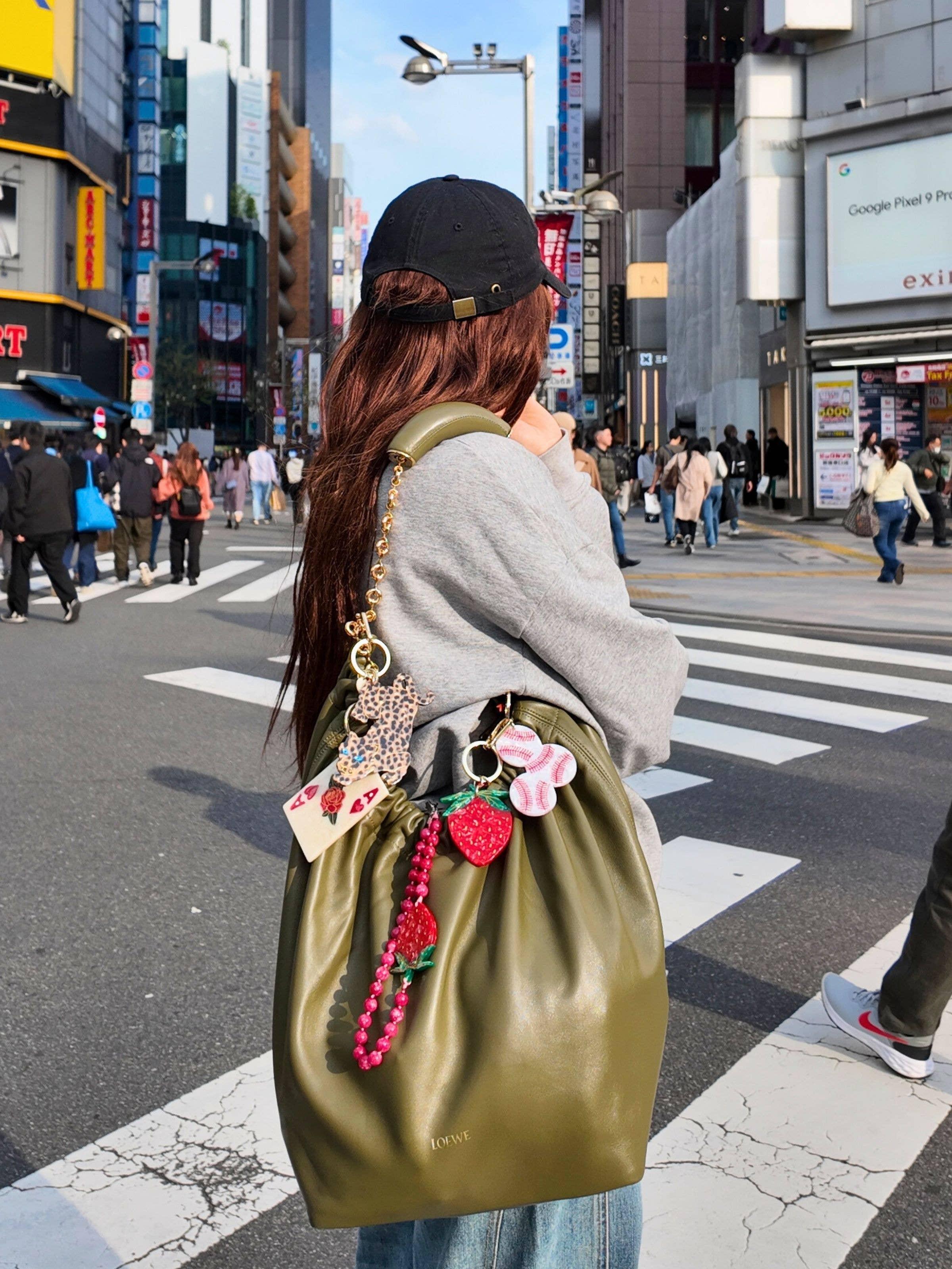 Loewe olive green leather bag with playful keychains, worn on city street