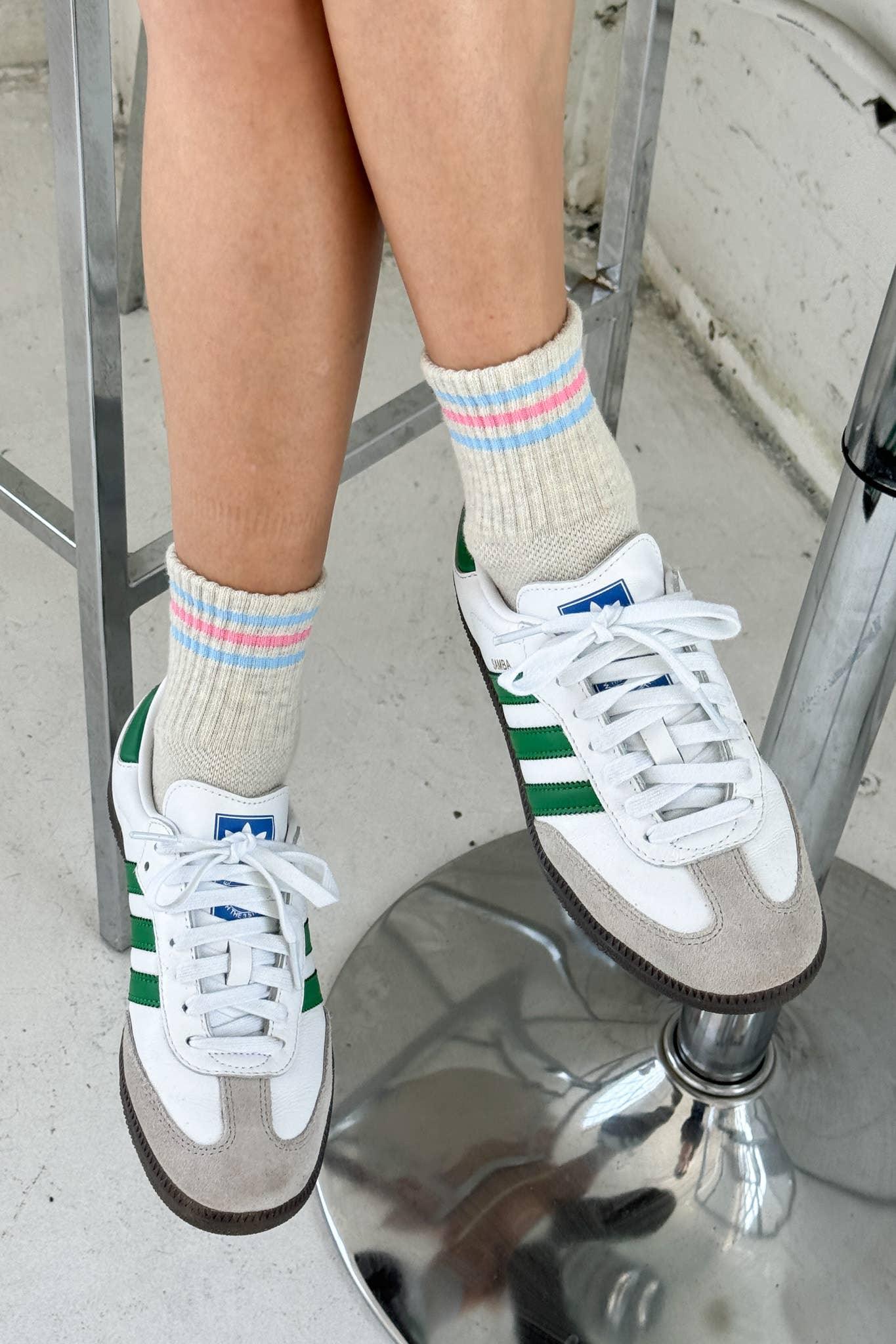 Adidas white leather and suede sneakers with green stripes on person wearing cream socks