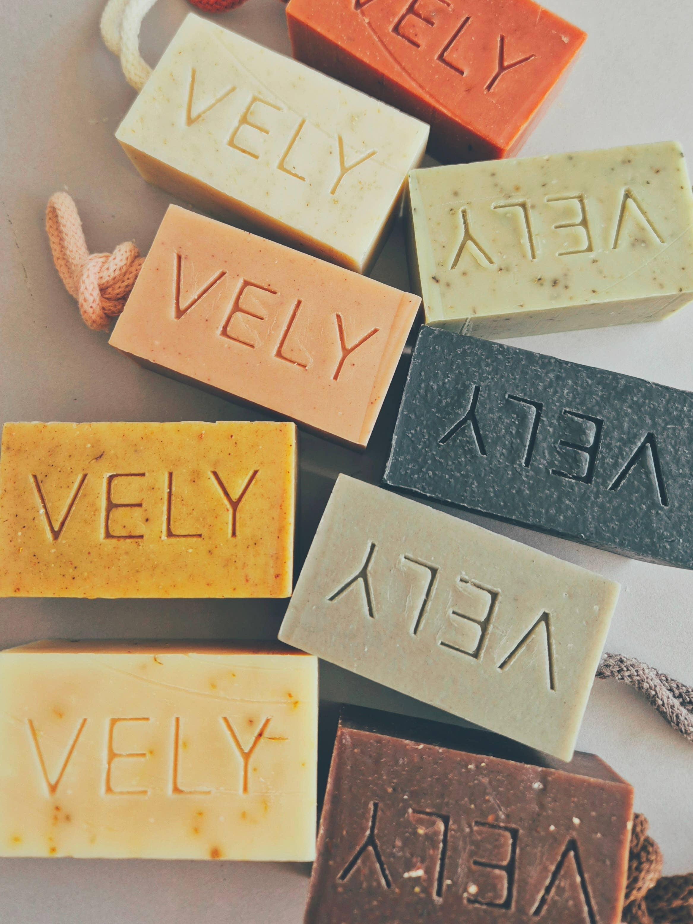 VELY brand artisanal soap bars in assorted natural colors and textures on light background