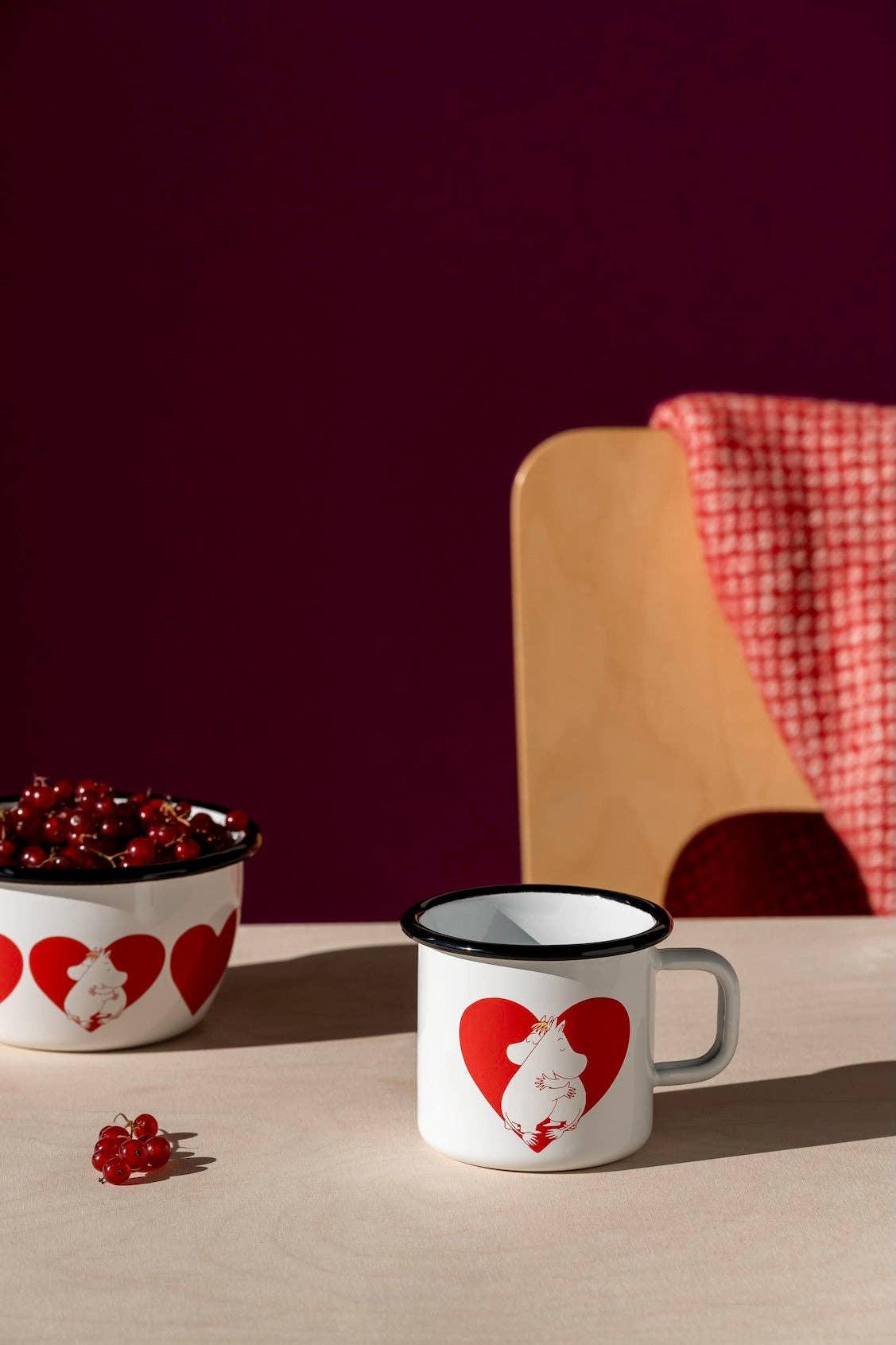 Muurla white enamel mug with red heart and Moomin illustration on light wood table.