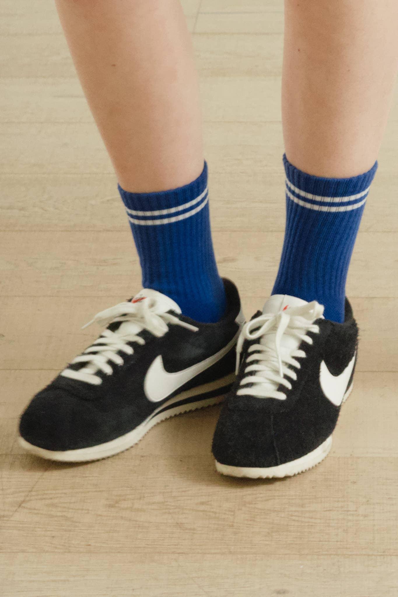 Nike black suede sneakers with white logo and blue ribbed socks on wooden floor
