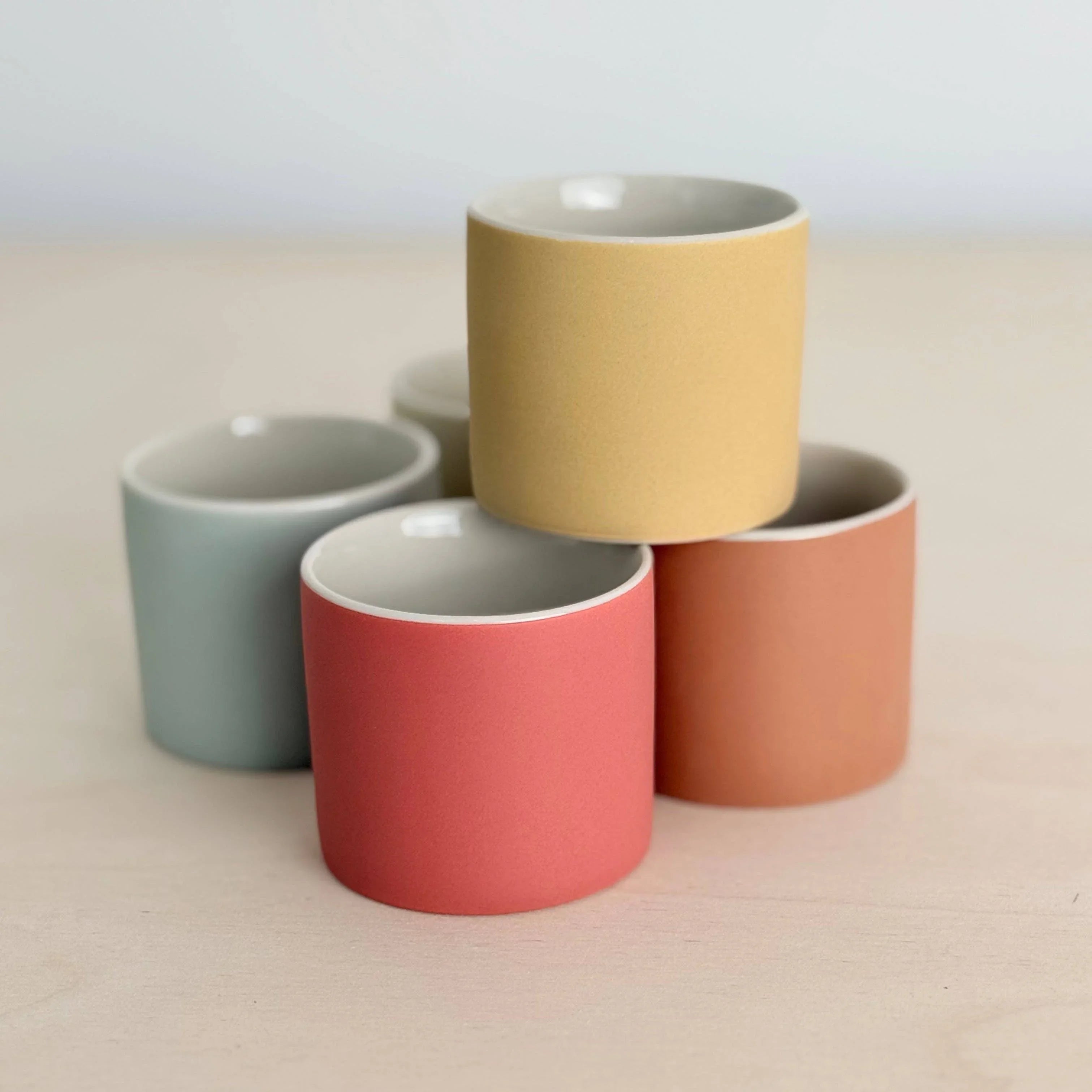 Studio Arhoj ceramic cups in pastel yellow, peach, pink, and blue on light wood surface
