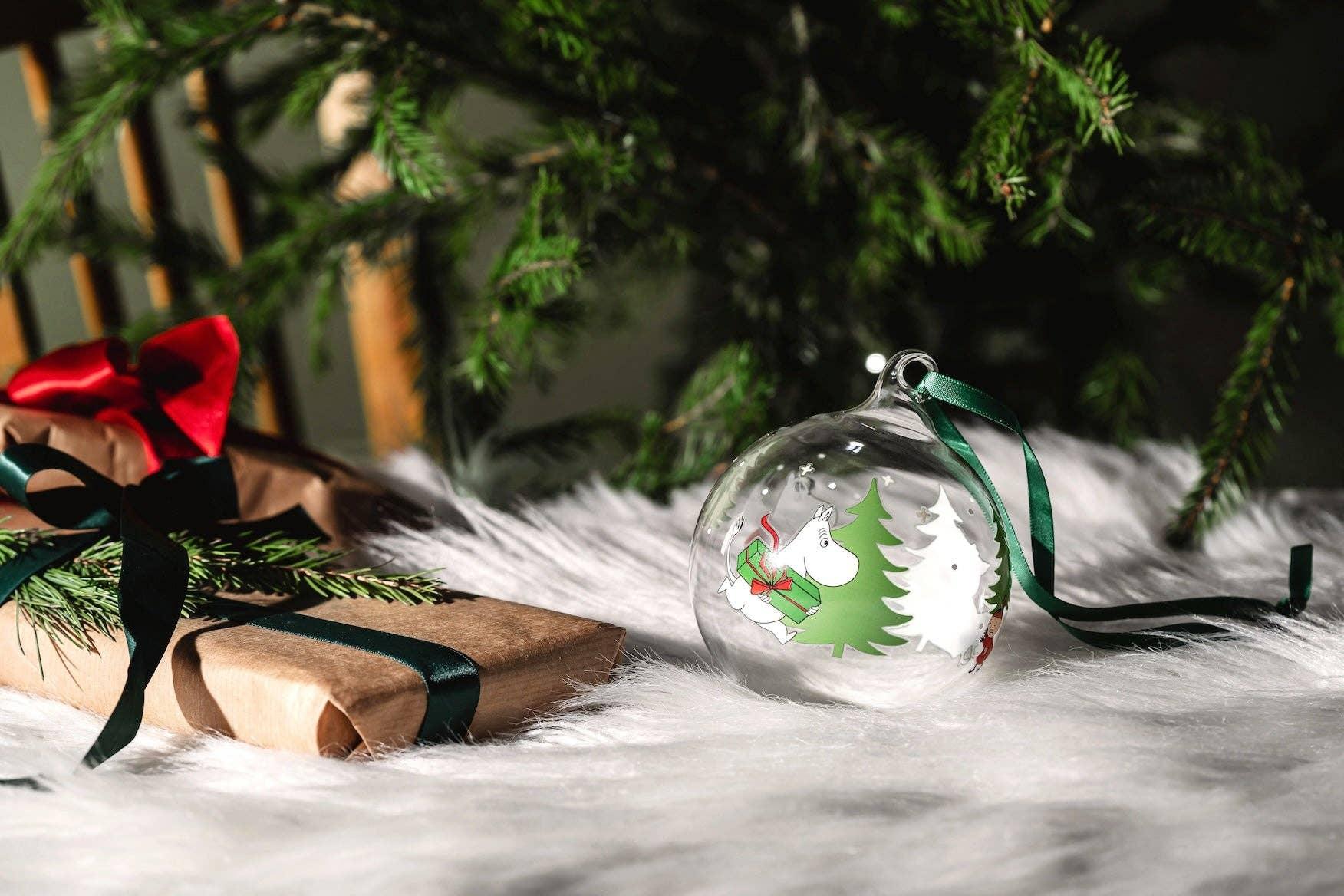 Moomin glass Christmas bauble with green tree and ribbon, beside wrapped gifts