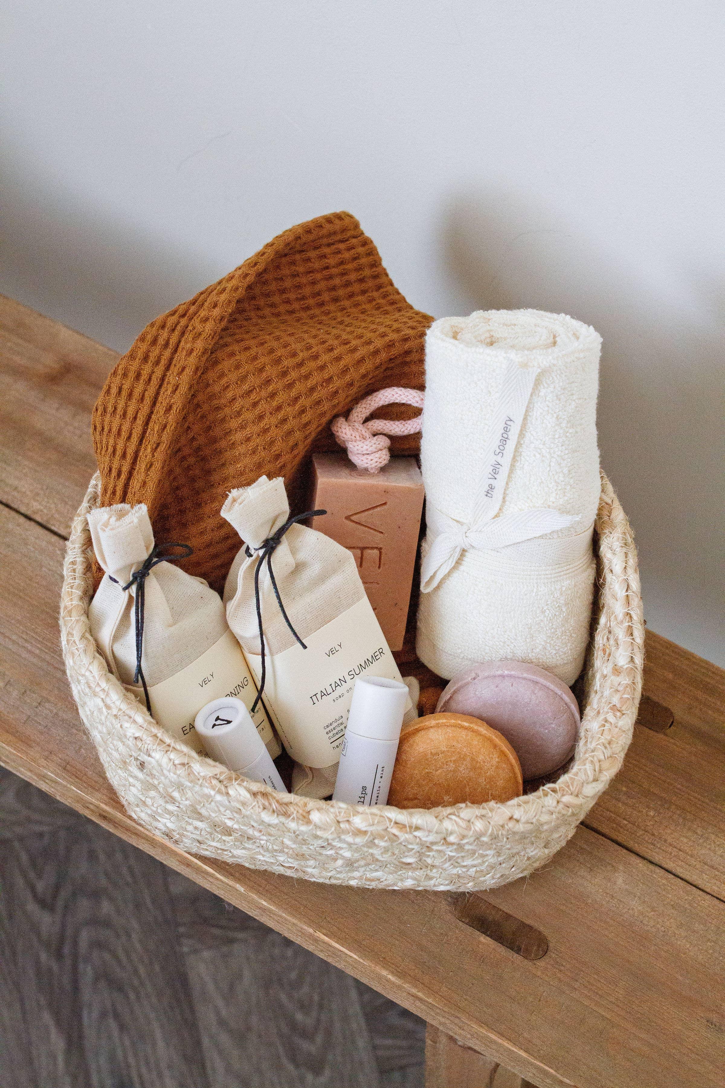 VELY gift basket with cotton towel, body care products, brown cloth, and soap on wooden table.