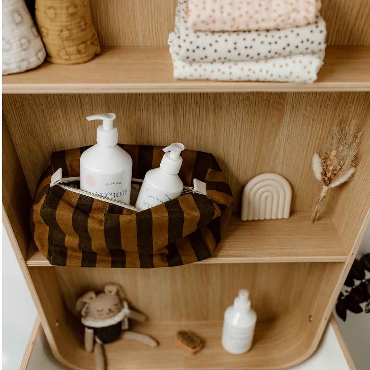 Minois Paris baby skincare bottles in striped canvas pouch on wood shelf with neutral decor