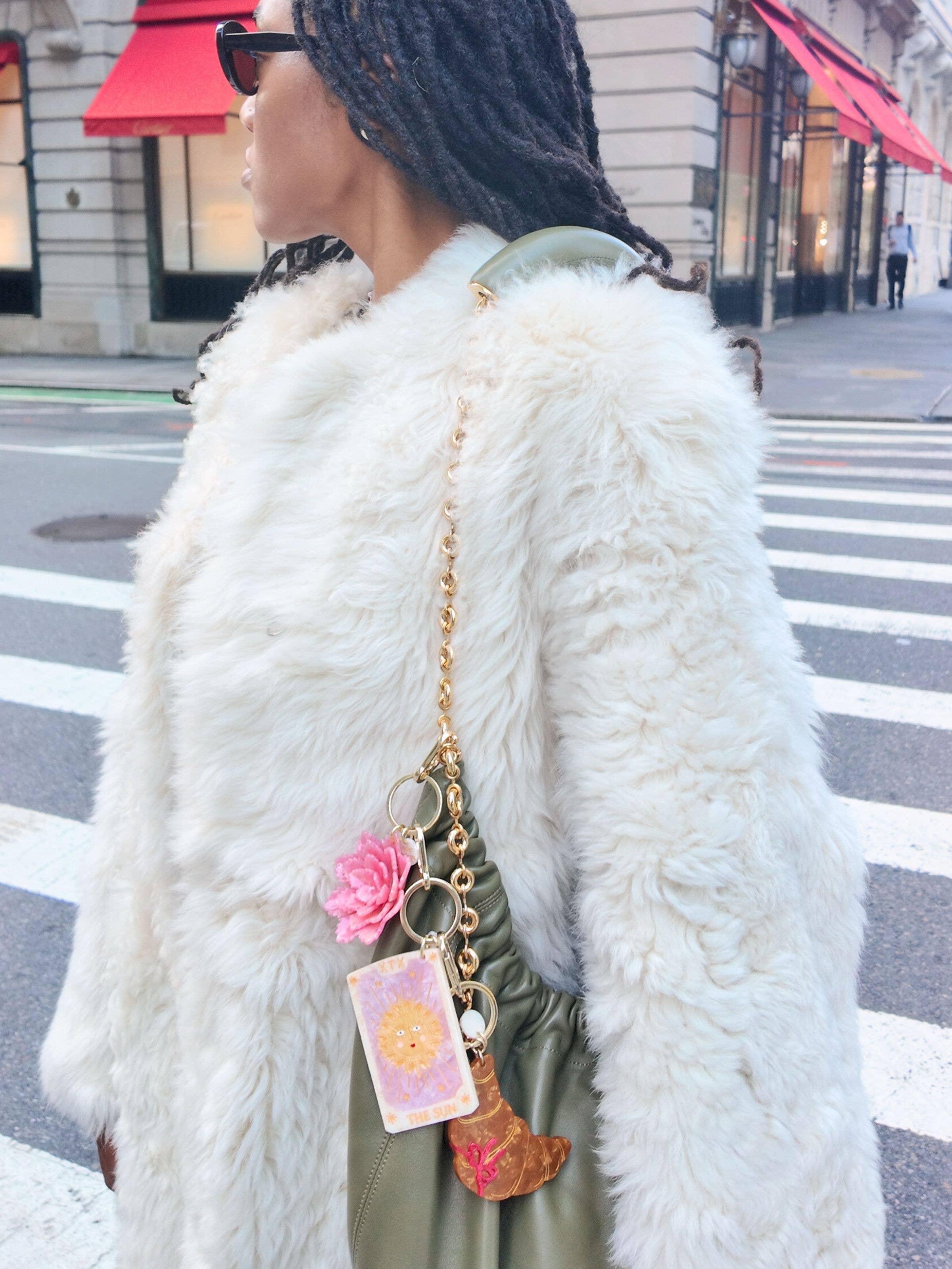 TITTY luxury handbag in green leather with gold chain, tarot and croissant charms, worn with a white faux fur coat.