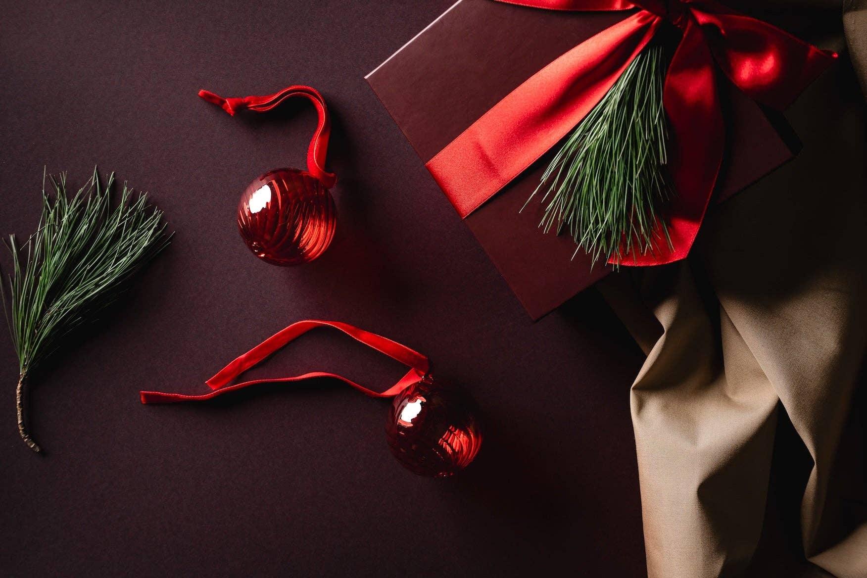 Premium gift box with red satin ribbon, pine sprig, red glass ornaments on a dark background