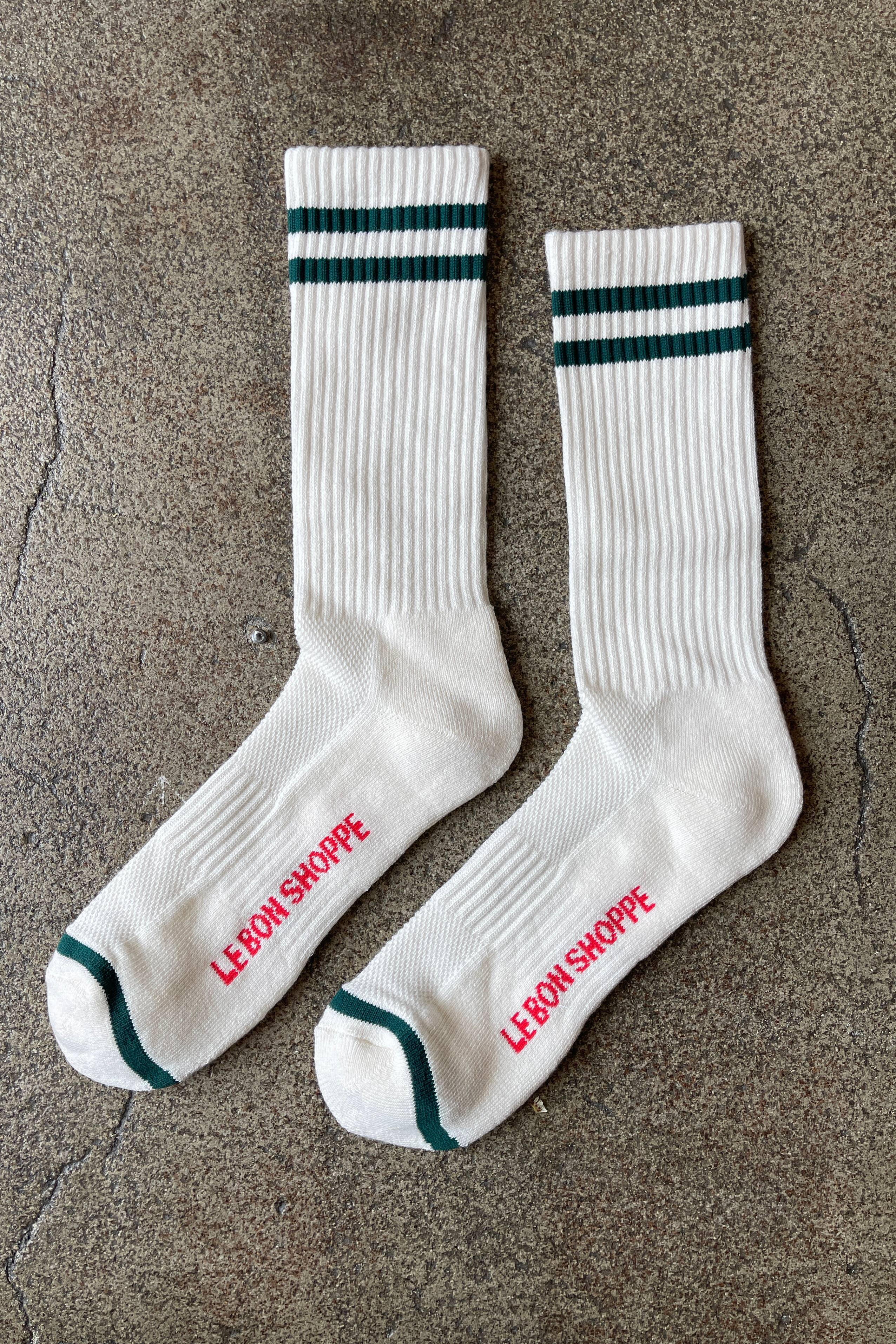 Le Bon Shoppe white ribbed cotton socks with green stripes and text logo, flat lay on stone