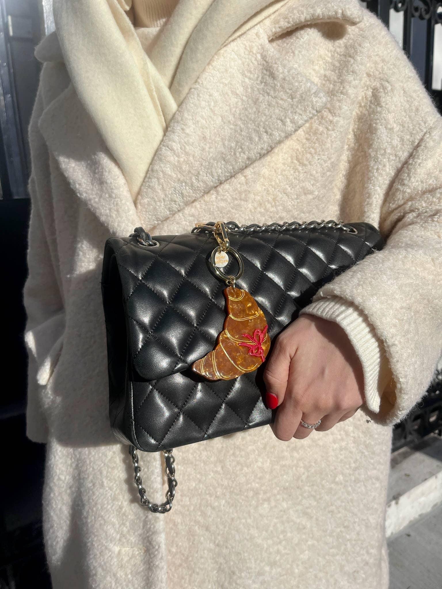 Macon & Lesquoy croissant brooch on black quilted leather handbag, cream wool coat