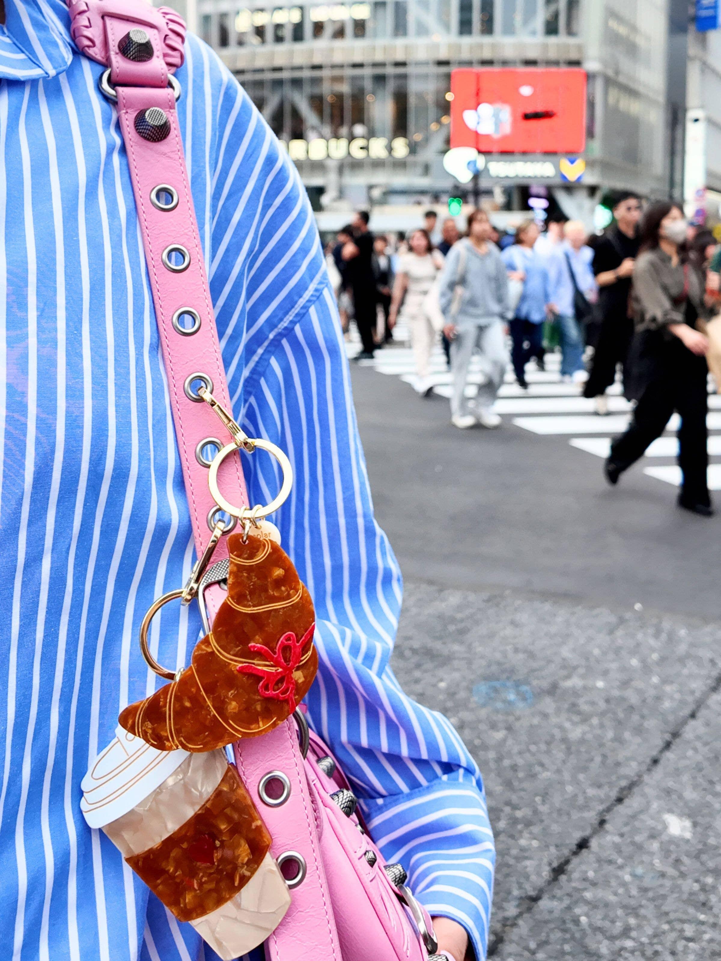 Dior croissant and coffee acrylic bag charm on pink leather strap, street style background.