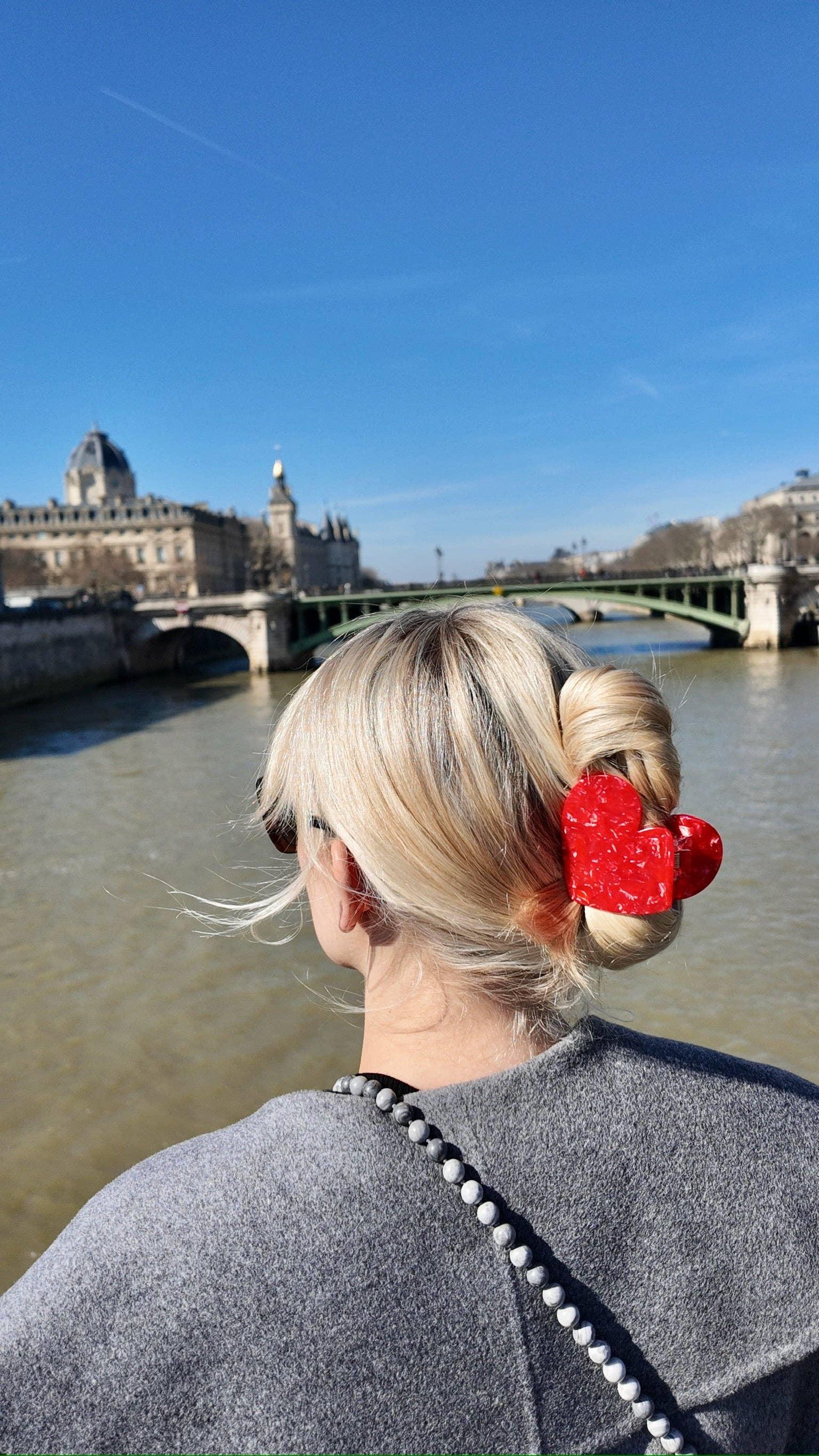 Valet Studio red acetate heart hair clip in blonde hair, river and cityscape background