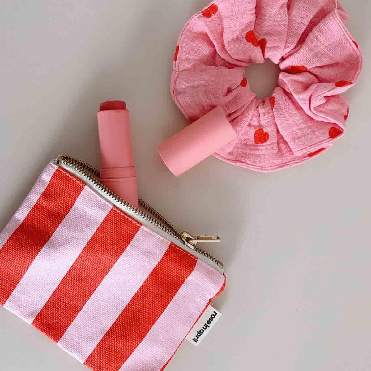 Pouch Australia striped fabric pouch, pink scrunchie, and pink lipstick on white surface