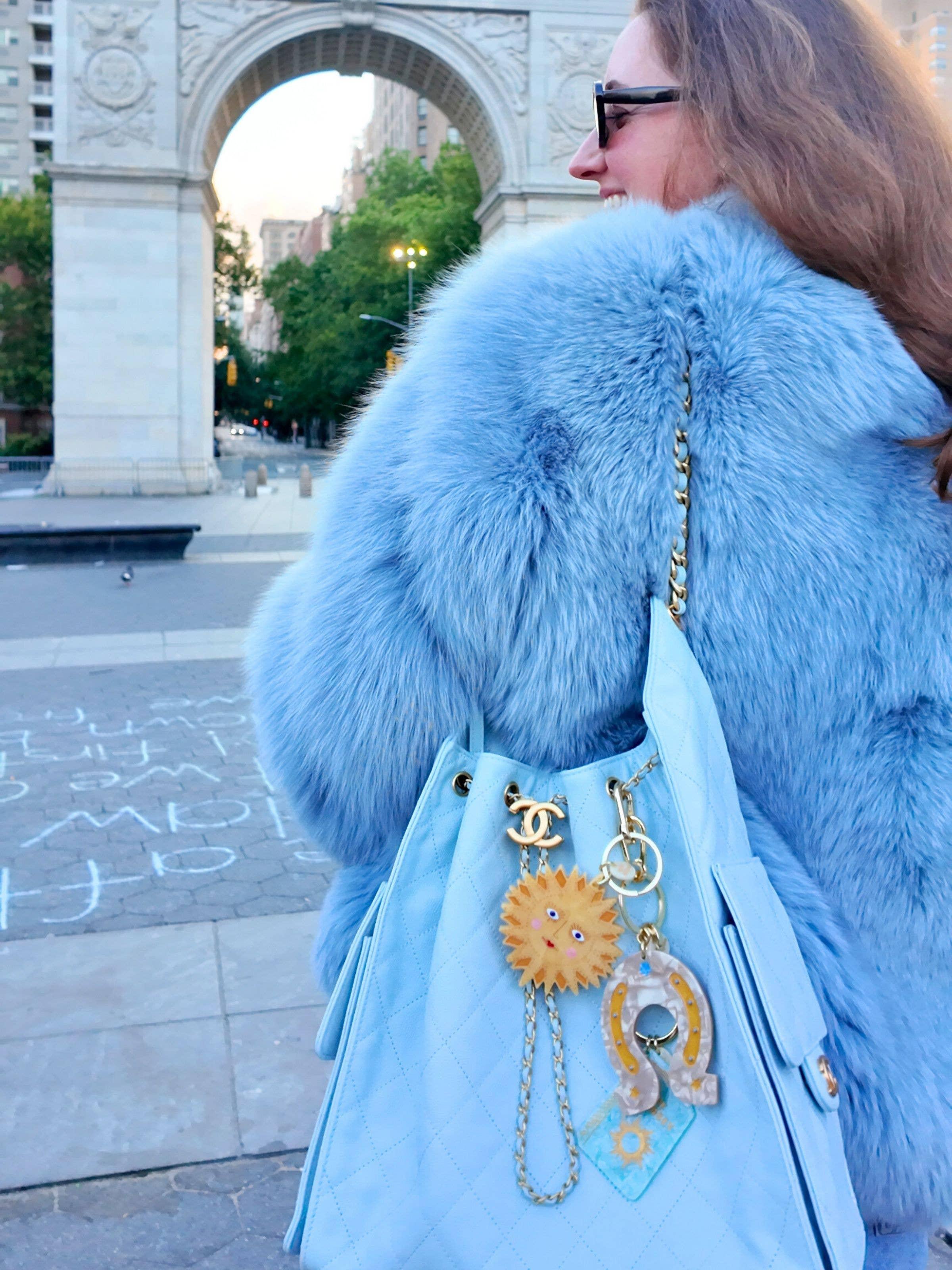 Chanel blue quilted leather bag with gold hardware, sun and horseshoe charms, worn with blue faux fur coat