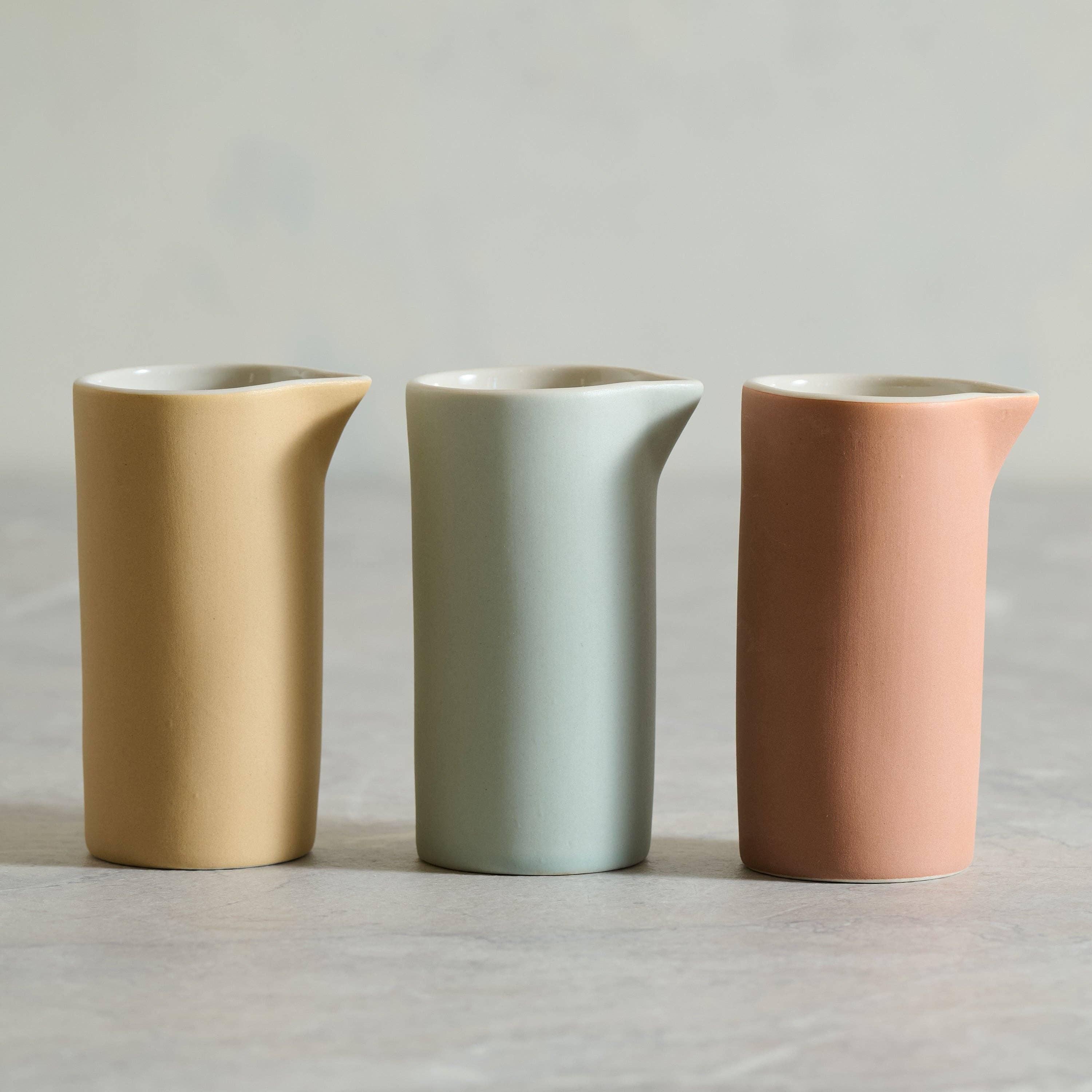 Ferm Living ceramic jugs in matte yellow, pale green, and terracotta on grey surface