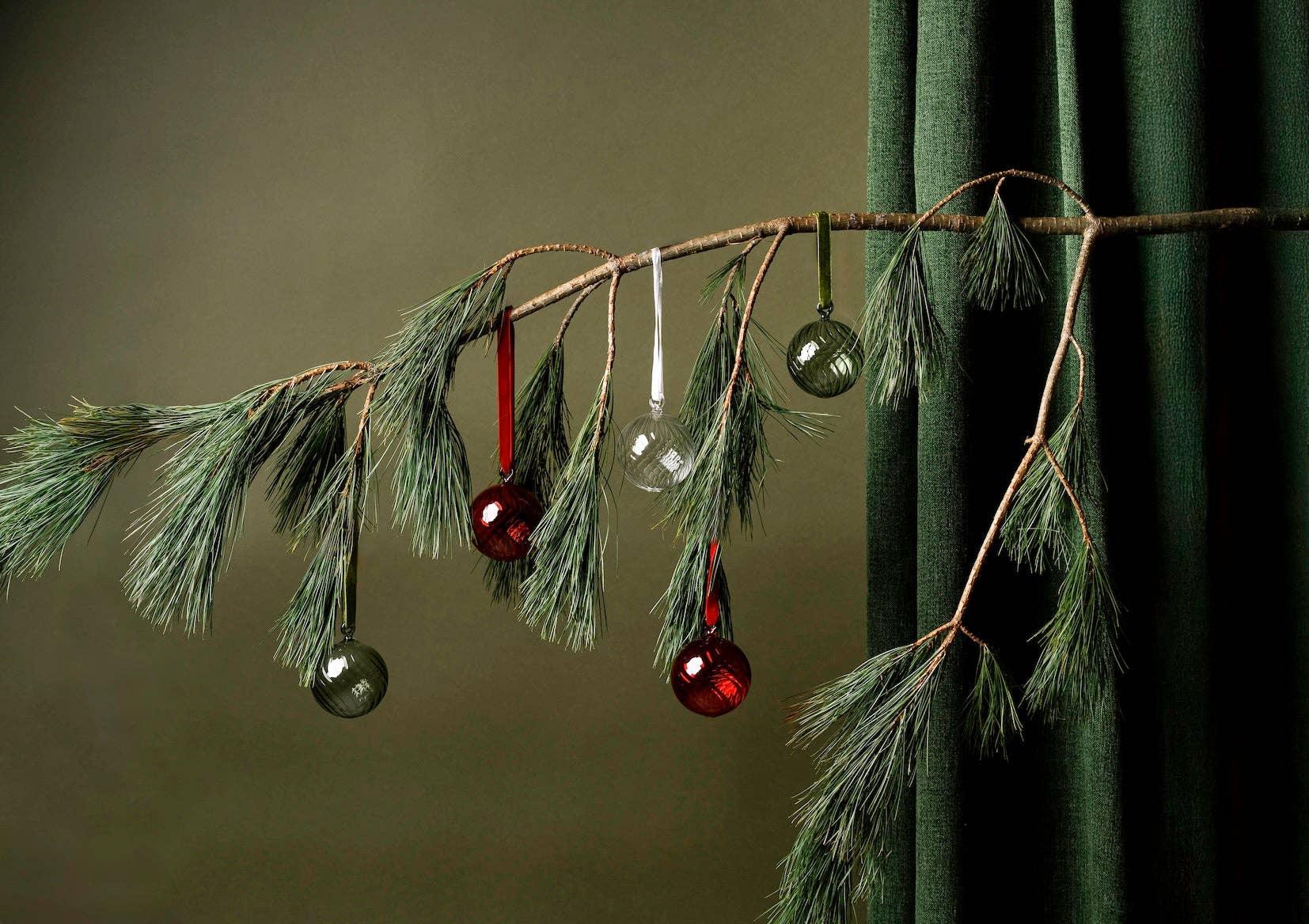 Ferm Living glass Christmas ornaments in red and green on pine branch, elegant green backdrop