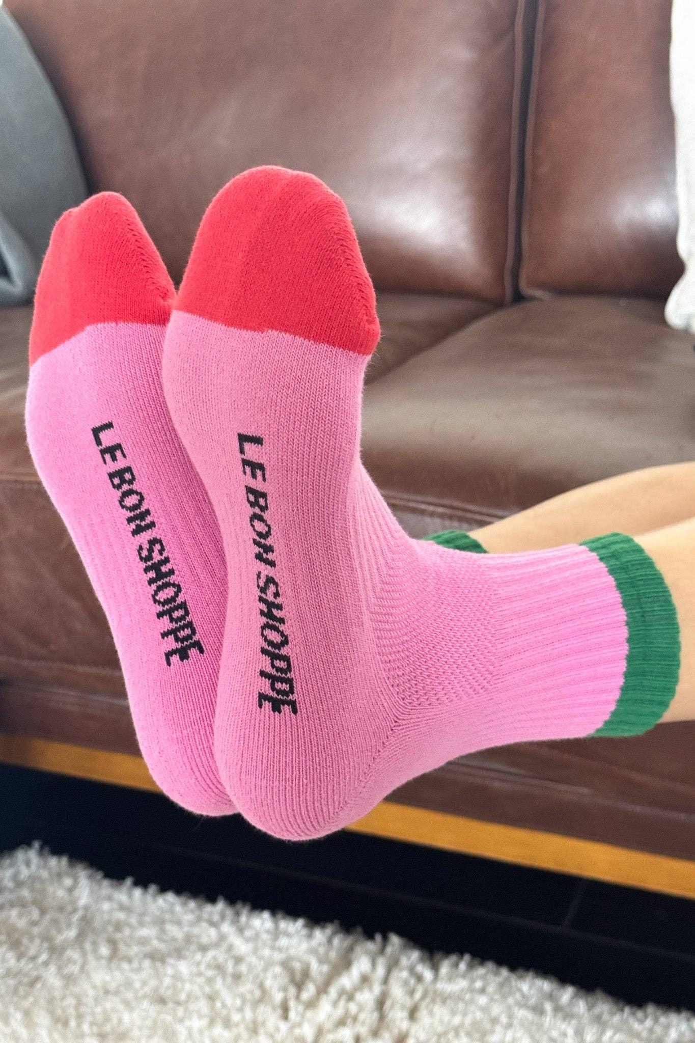 Le Bon Shoppe pink cotton socks with red toes and green trim on a sofa background