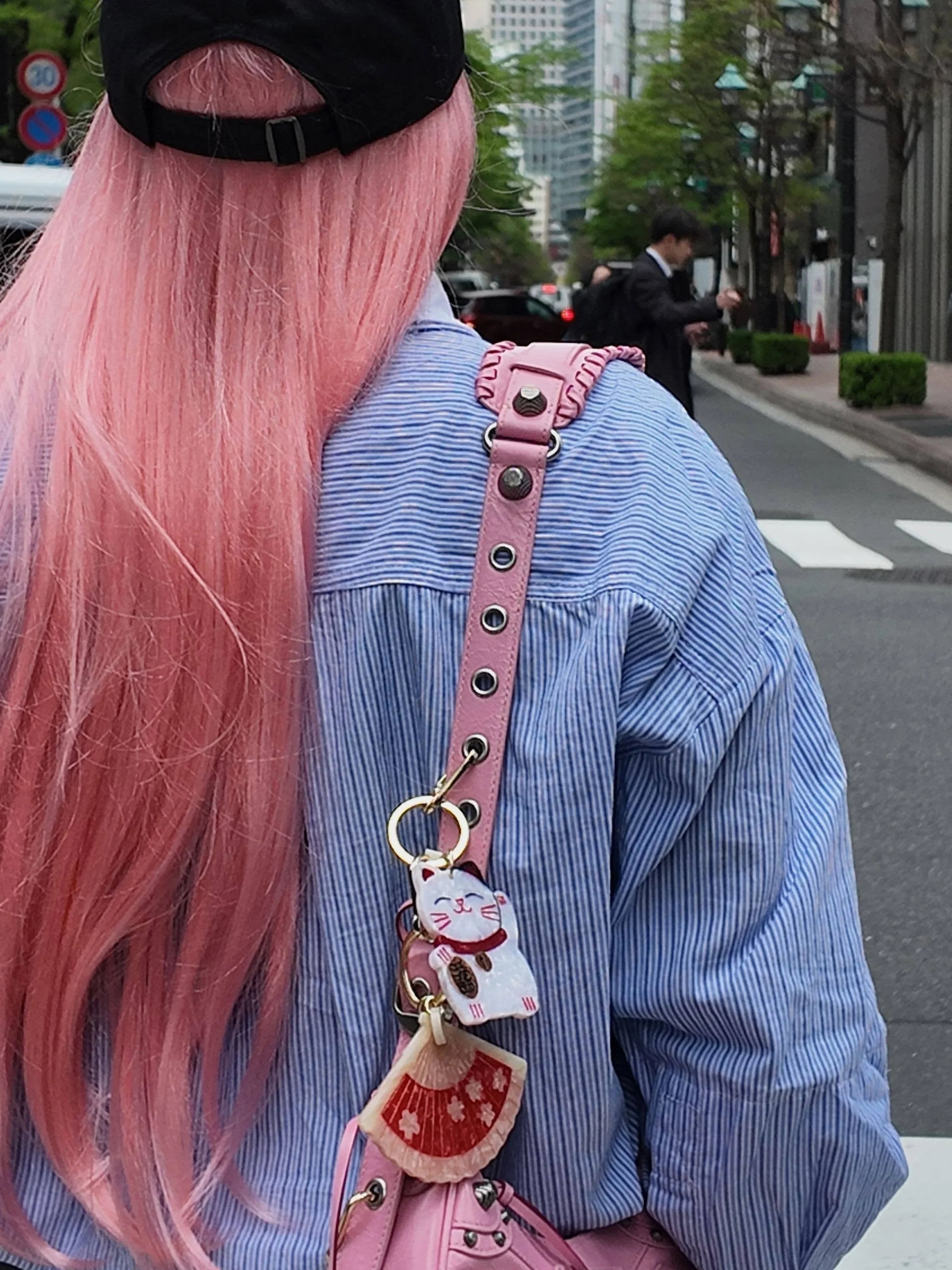 Person with pink hair and striped blue shirt carrying pink bag with maneki-neko cat charm