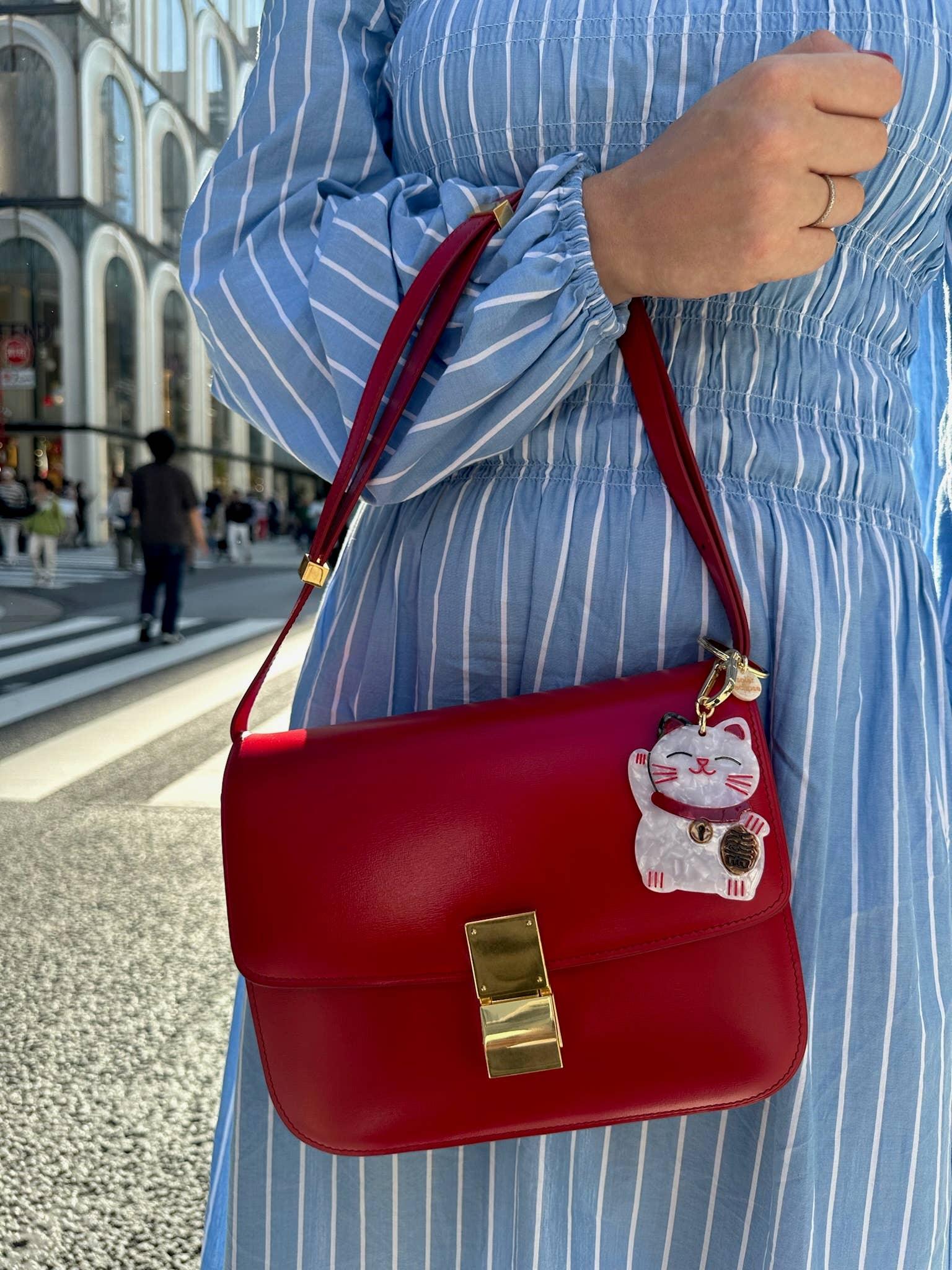 Celine red leather shoulder bag with gold hardware and lucky cat charm, worn with blue dress