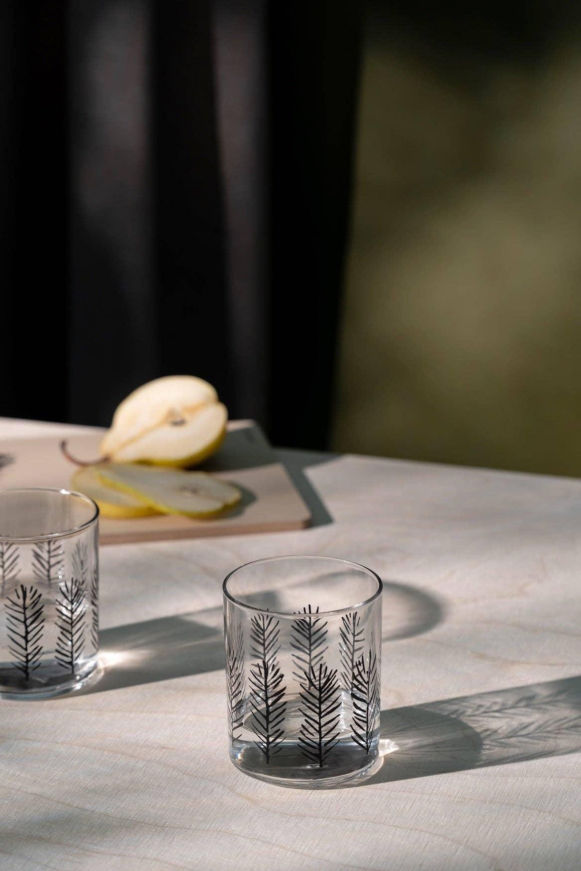 SiiZU clear glass tumbler with black botanical pattern on light table, sliced pear in background