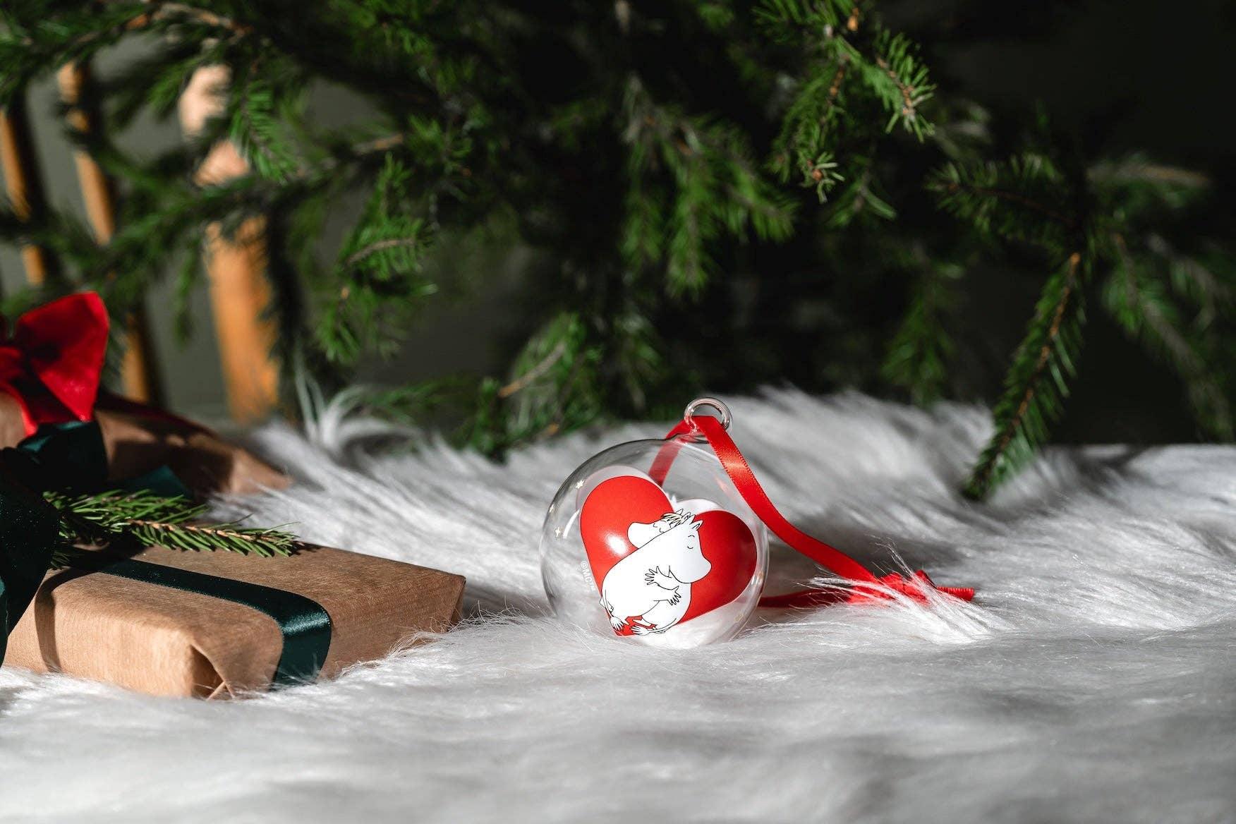 Moomin glass Christmas bauble with red heart and white ribbon on faux fur, gift box nearby