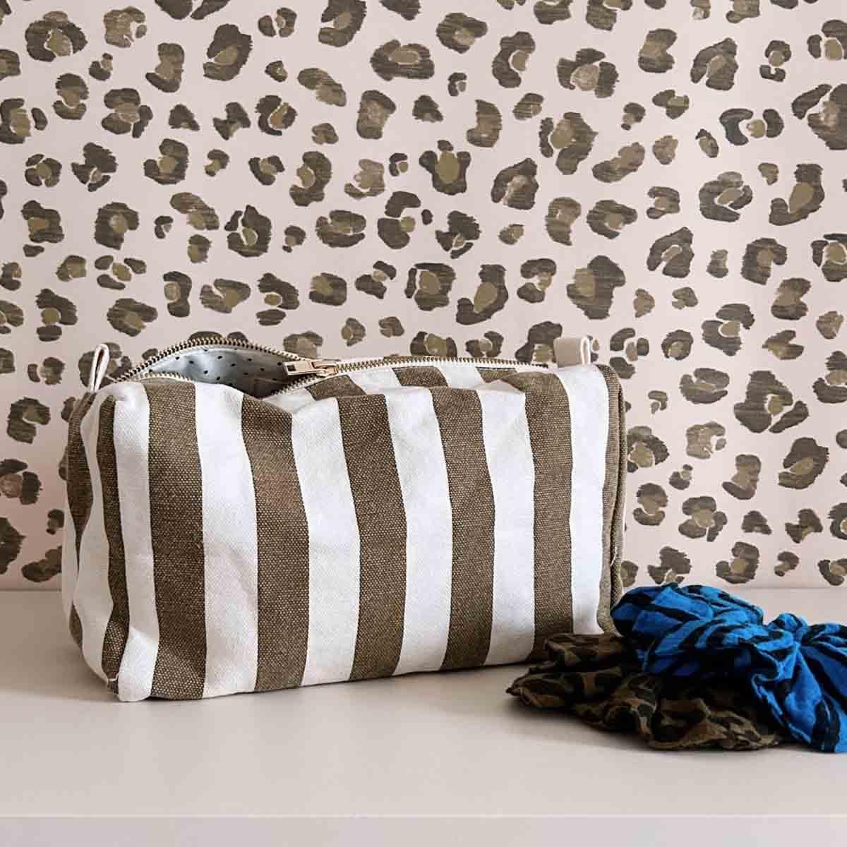 Baggu canvas striped toiletry bag in white and olive with hair scrunchies on beige table