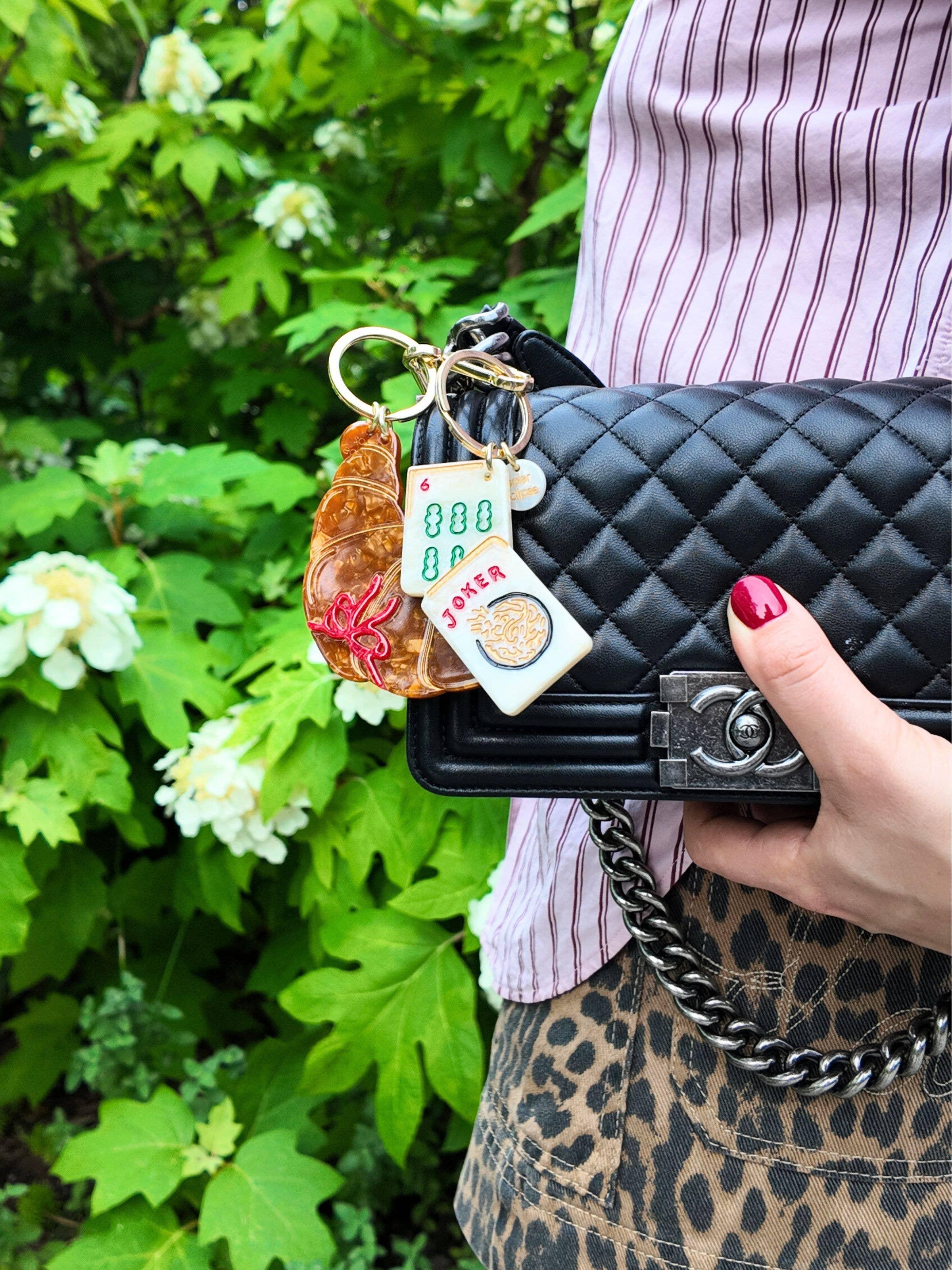 Chanel black quilted leather bag with gold Mahjong tile keychain, outdoors