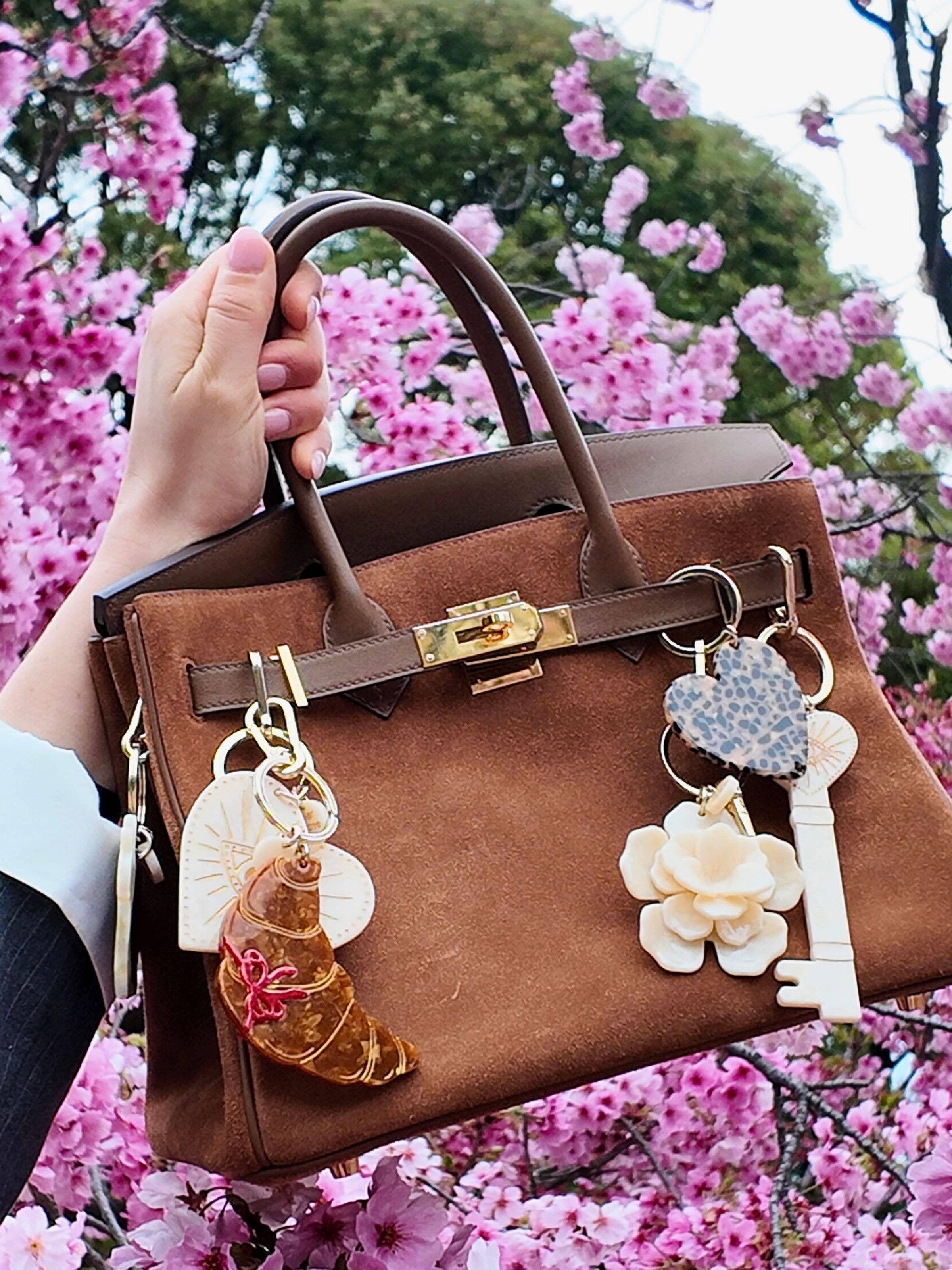 Hermès brown suede handbag with gold hardware and artisan keychains, cherry blossoms background